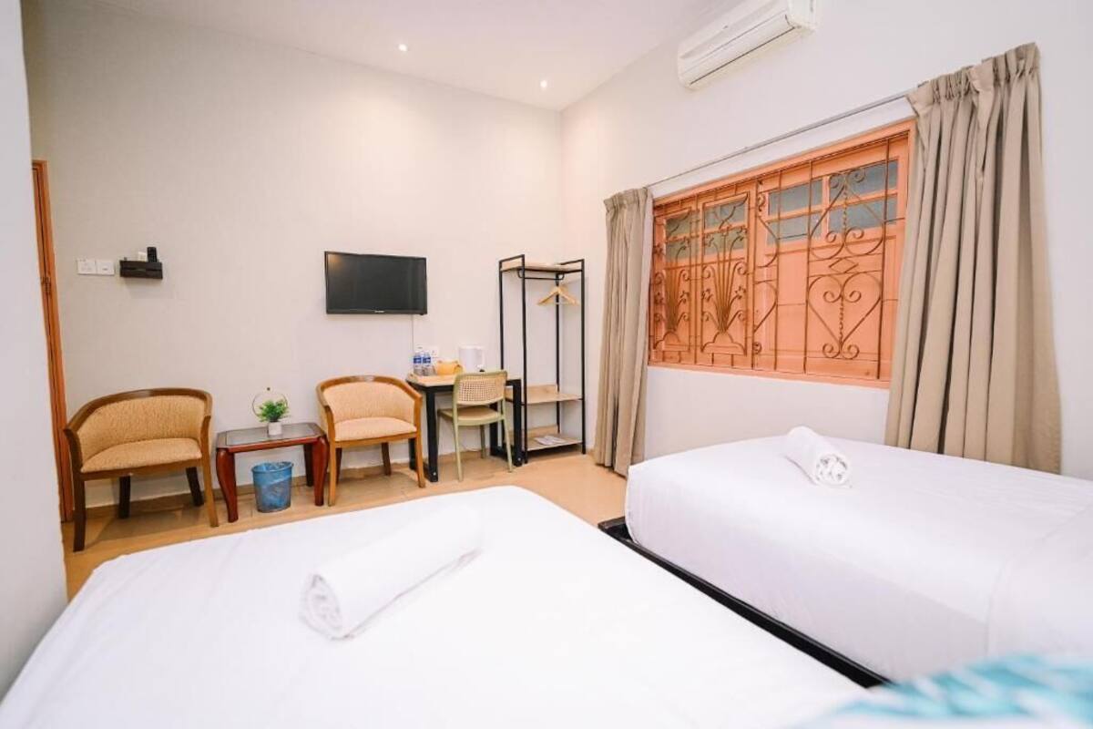 Habitación de hotel con dos camas, un escritorio, sillas, un televisor y una ventana con cortinas.