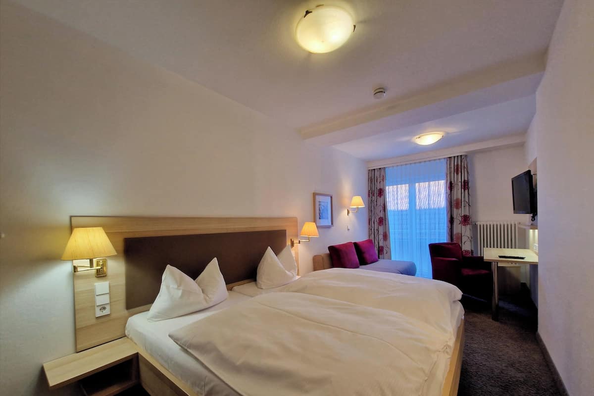 Une chambre d’hôtel avec un grand lit, des lampes de chevet, un bureau avec une chaise, une télévision et une fenêtre avec des rideaux.