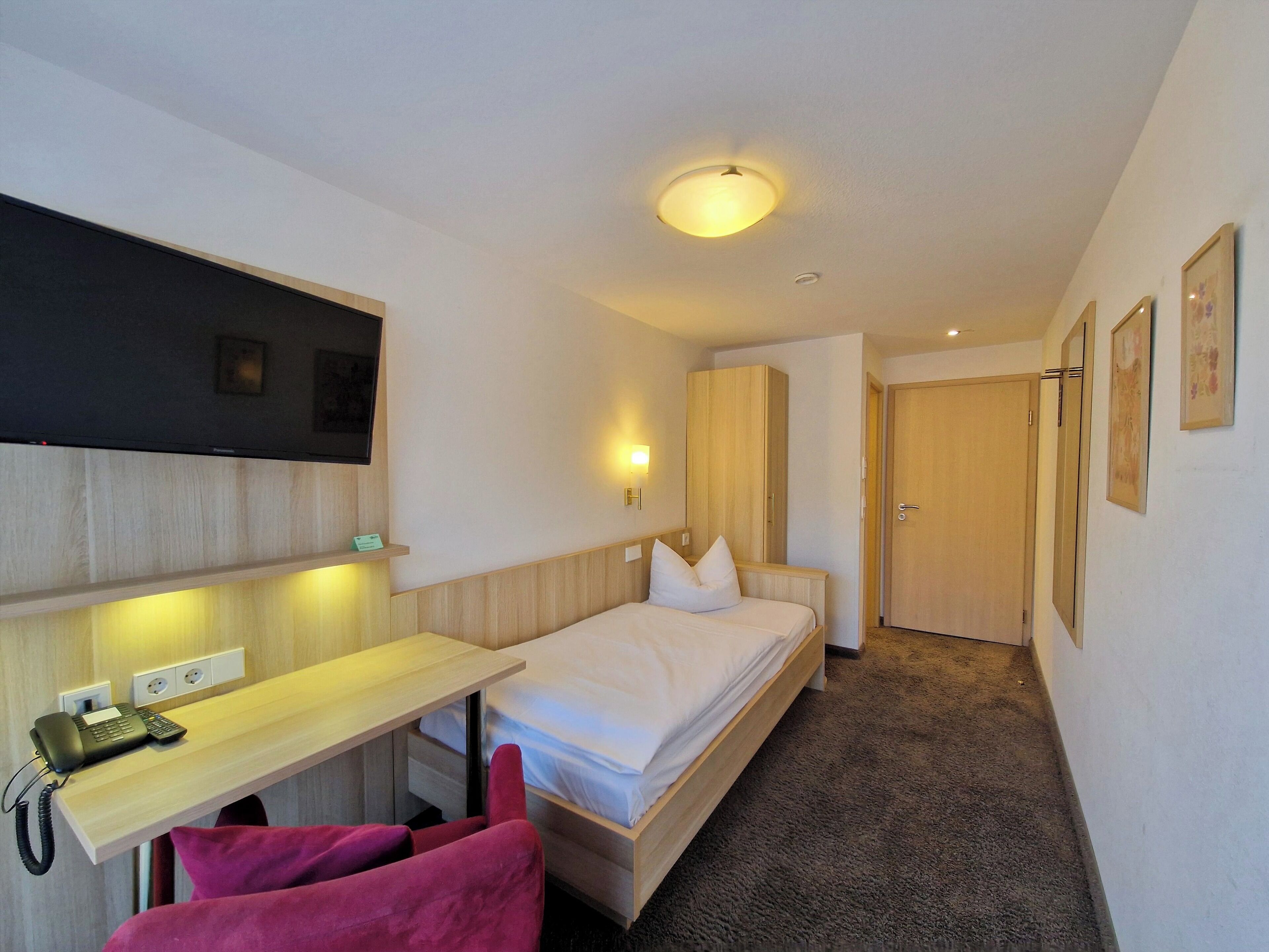 Ein Hotelzimmer mit einem Bett, einem Schreibtisch mit Telefon, einem Stuhl, einem Kleiderschrank und einer Tür.