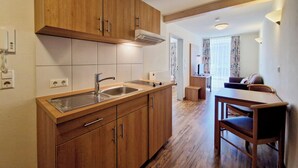 A modern kitchen with wooden cabinets, a built-in sink, and a dining area with a table and chairs. - Blume Hausach I Hotel & Restaurant (Hausach)