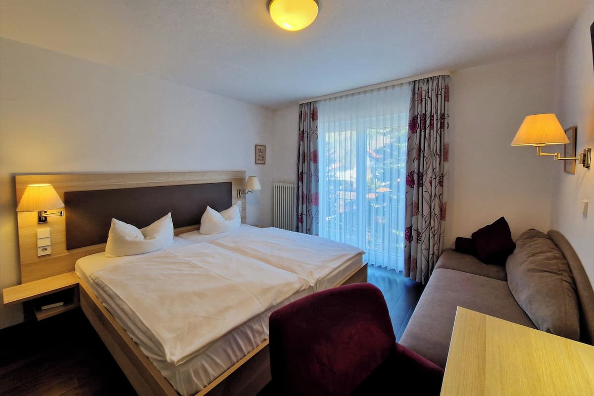 Une chambre d’hôtel avec un grand lit, un canapé, une petite table et une fenêtre avec des rideaux.
