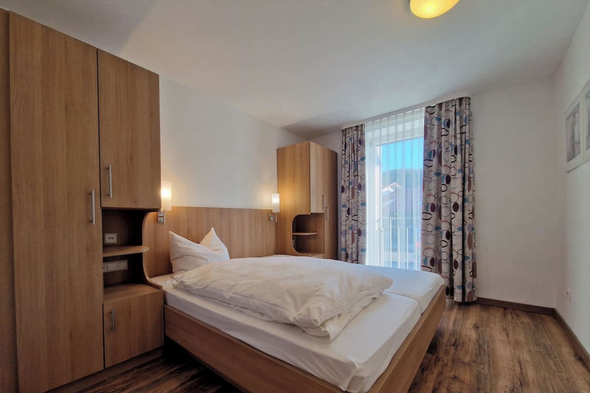 Une chambre moderne avec un lit en bois, une armoire intégrée et une grande fenêtre avec des rideaux.