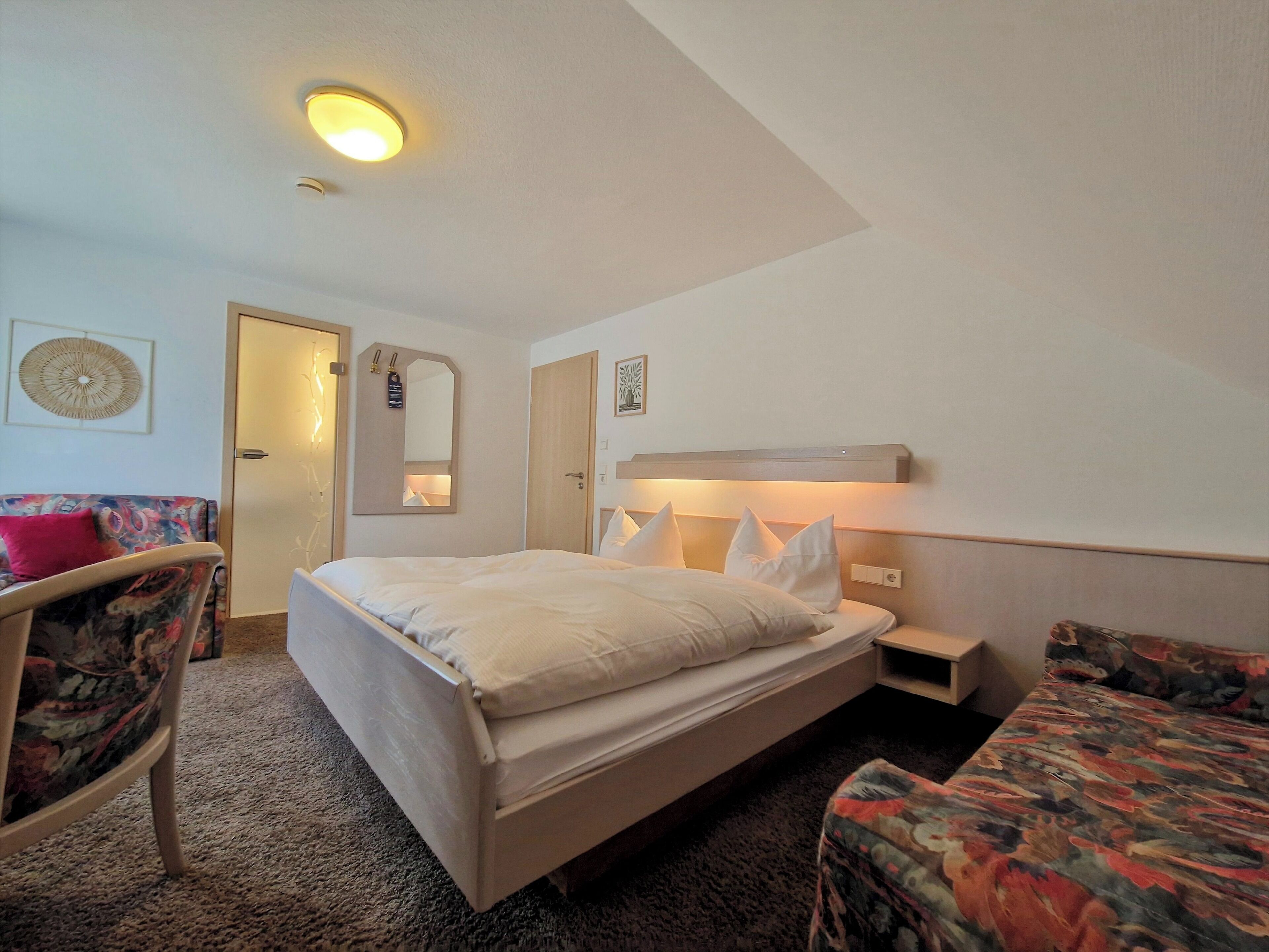 Une chambre d’hôtel comprenant un lit, deux chaises, une table de chevet, un miroir et un luminaire au plafond.