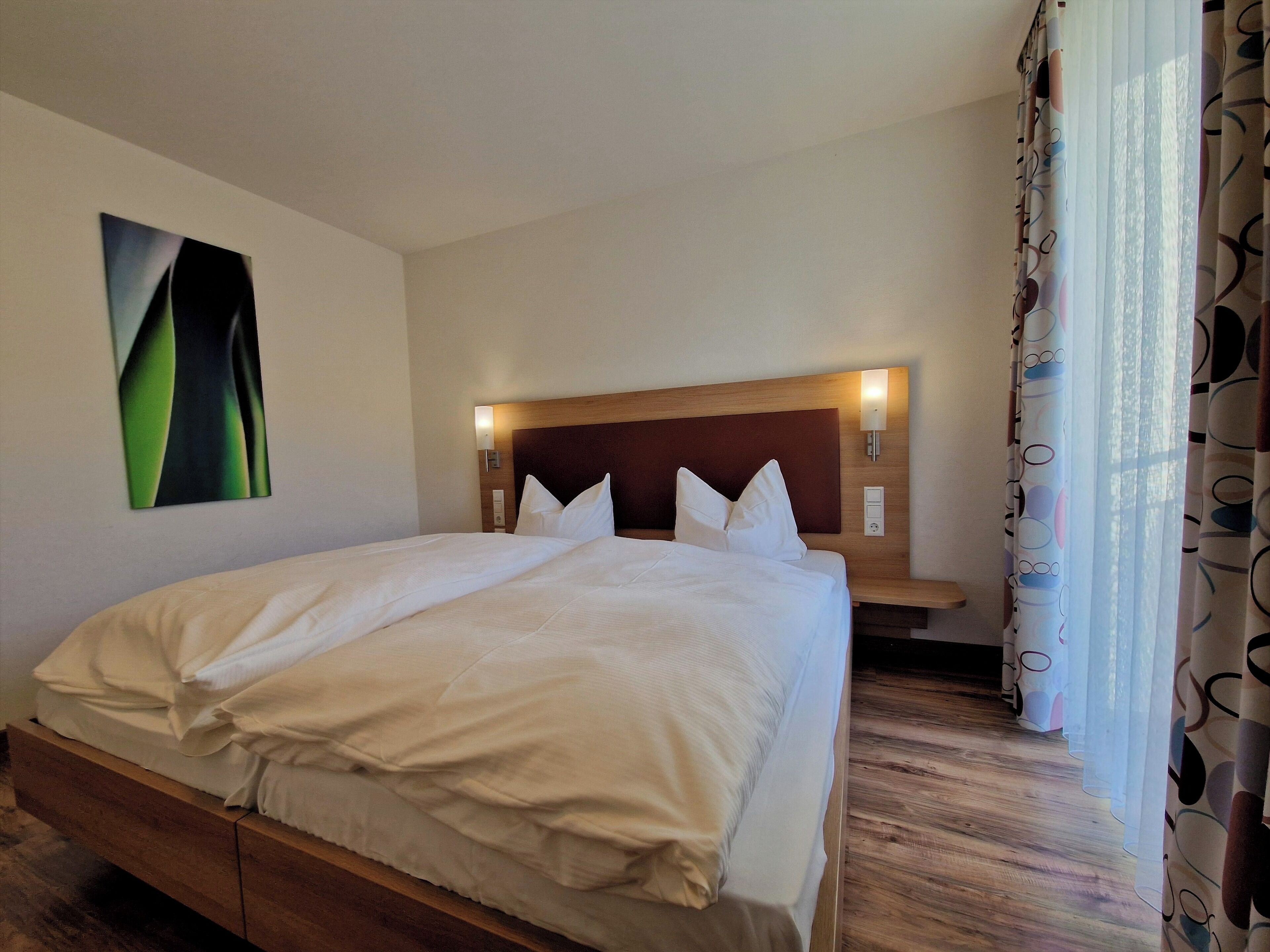 A neatly made bed with white linens, a wooden headboard, and two bedside lamps.