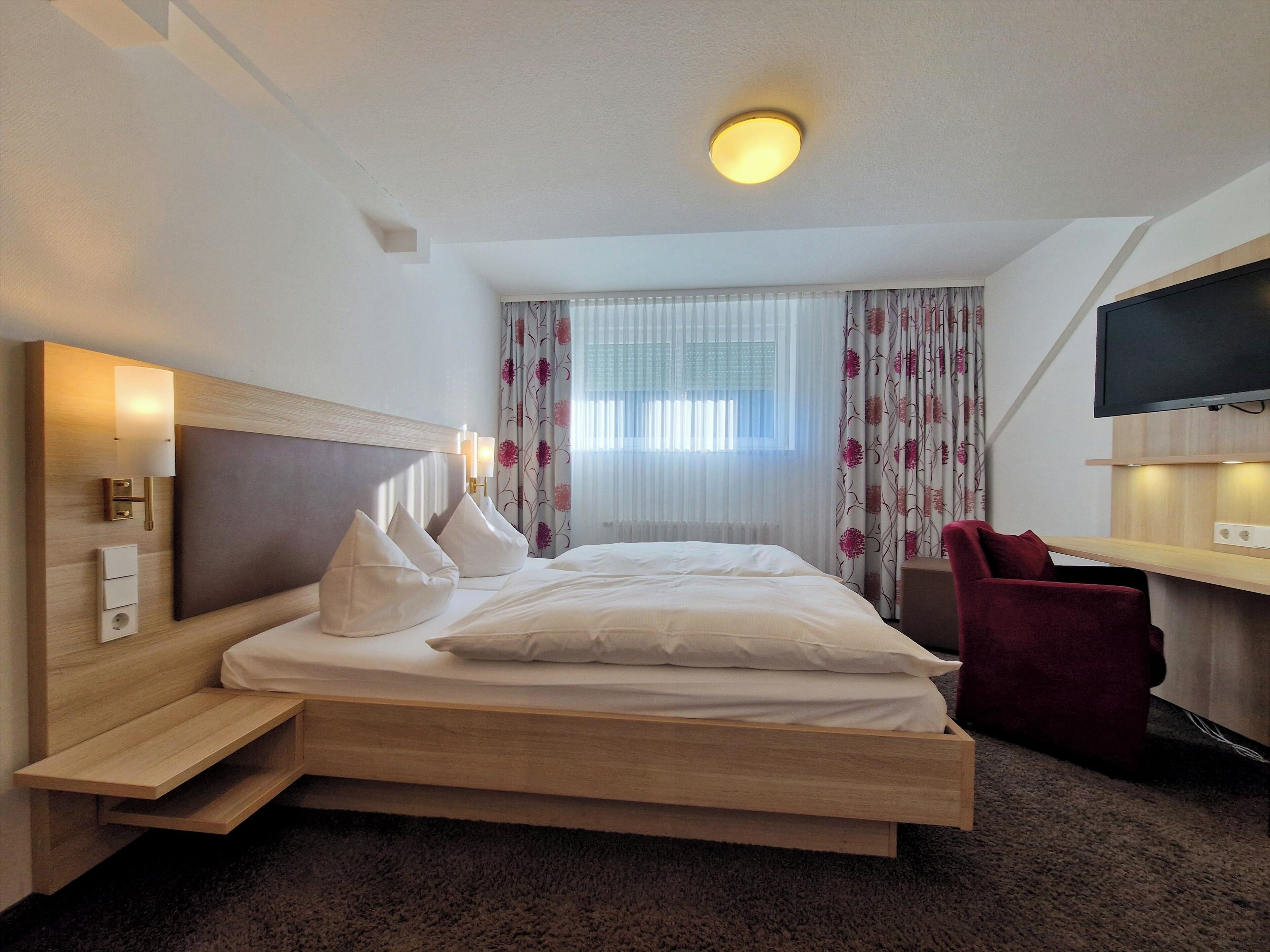 A hotel room with a bed, bedside table, TV, and curtains.