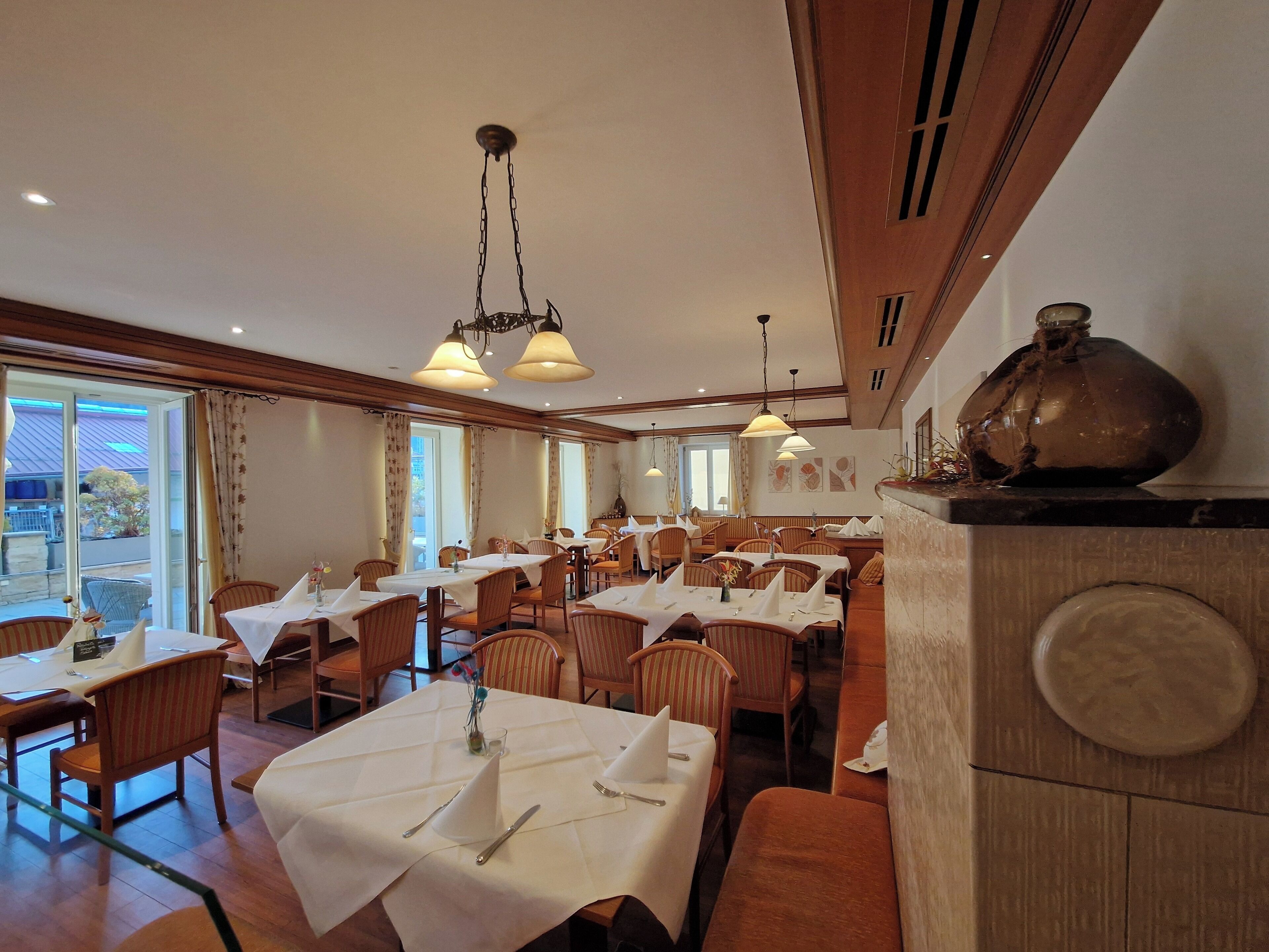 A restaurant with multiple tables, wooden chairs, and hanging pendant lights.