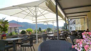 An outdoor patio area with tables and chairs under large umbrellas, surrounded by potted plants and flowers. - Blume Hausach I Hotel & Restaurant (Hausach)