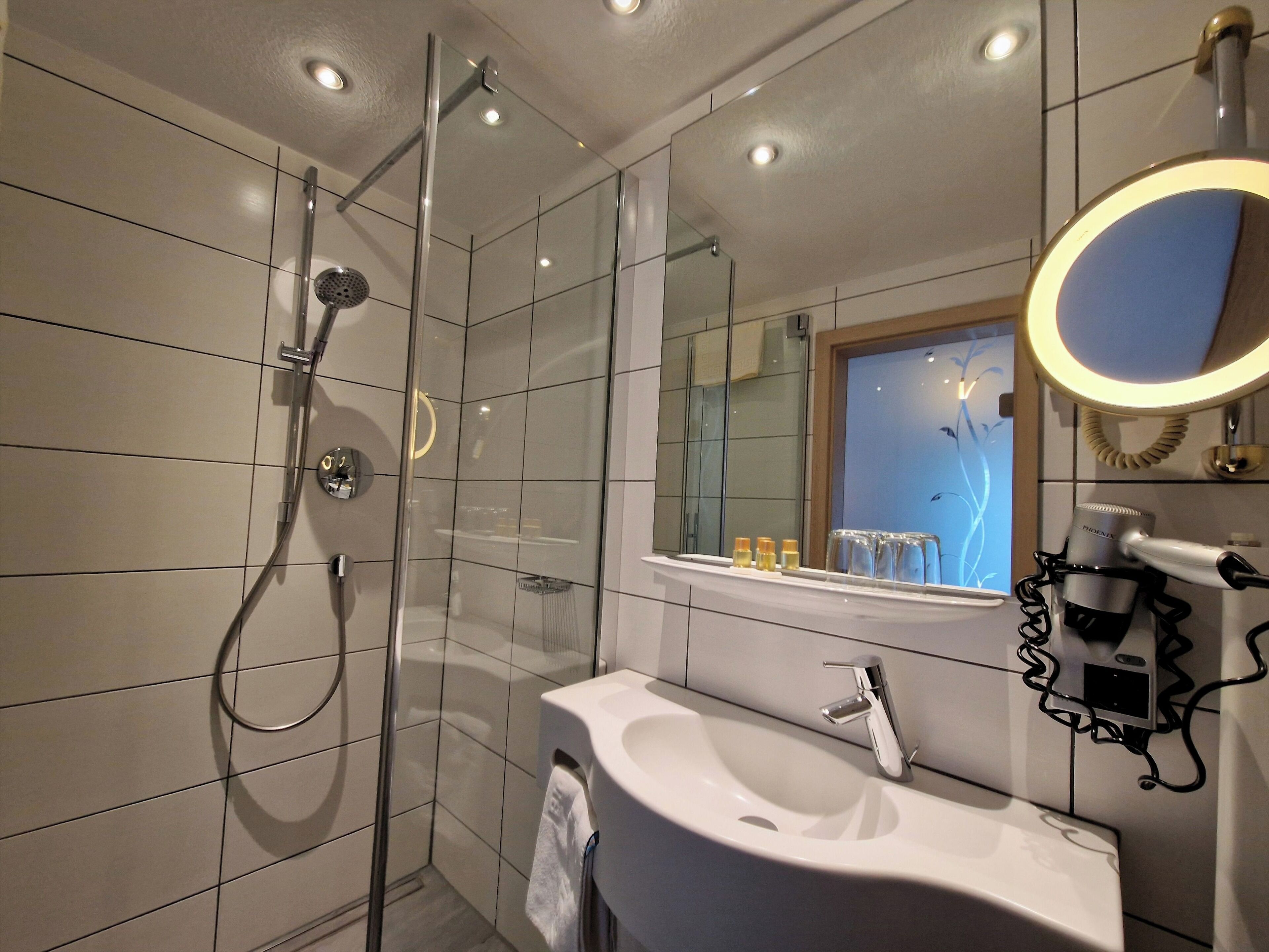 A modern bathroom with a glass-enclosed shower, a white sink, and a mirror with a round frame.
