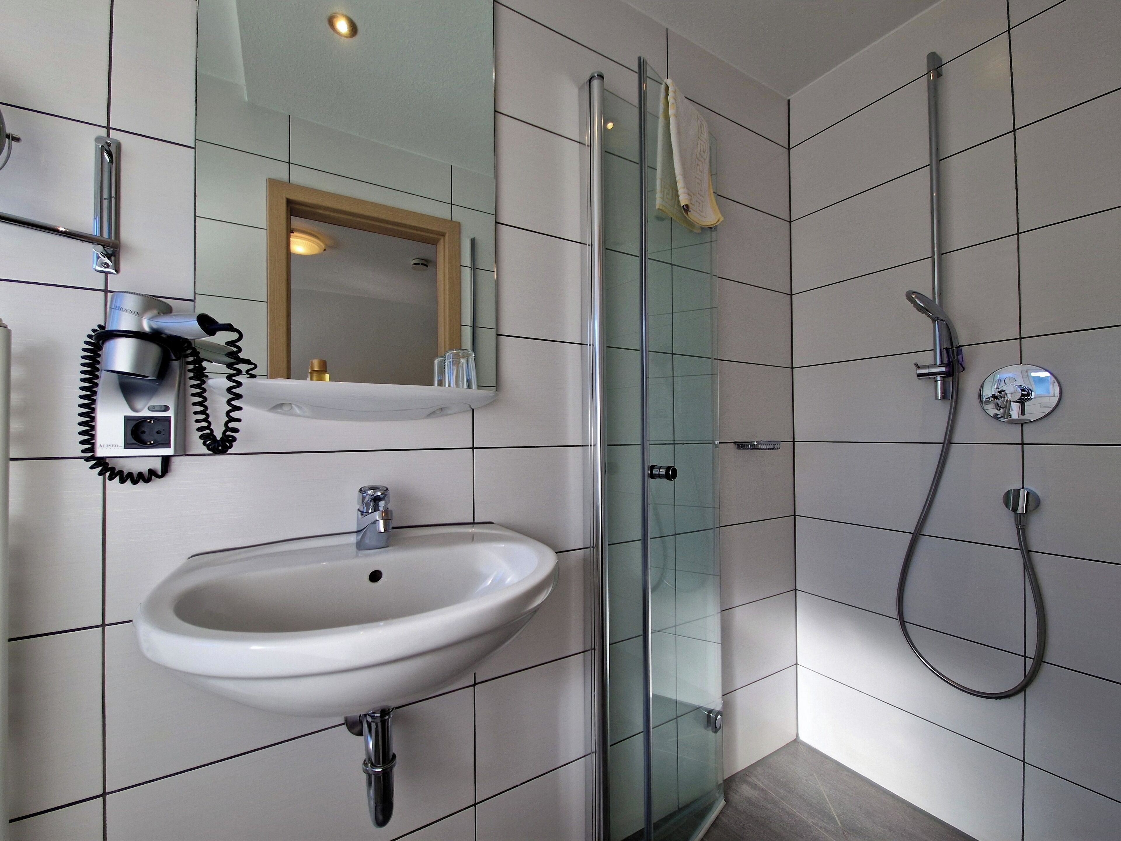A modern bathroom with a glass shower enclosure, a white sink, and a hairdryer mounted on the wall.