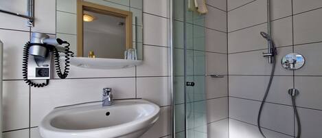 A modern bathroom with a glass shower enclosure, a white sink, and a hairdryer mounted on the wall.