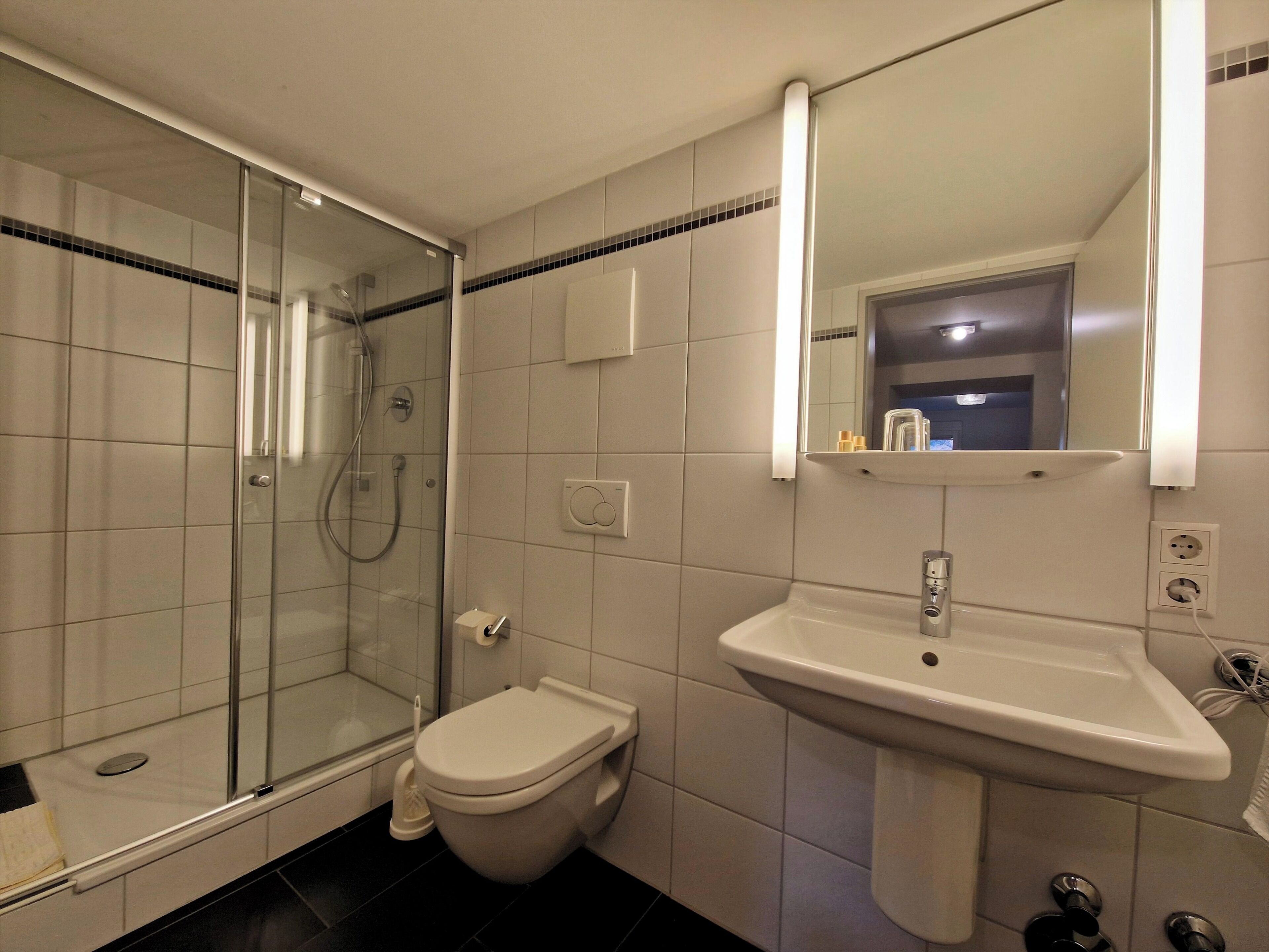 Un baño con ducha de vidrio, inodoro y lavamanos con espejo superior.