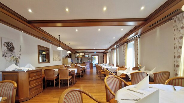 A hotel dining area with wooden furniture, white tablecloths, and a long counter. - Blume Hausach I Hotel & Restaurant (Hausach)