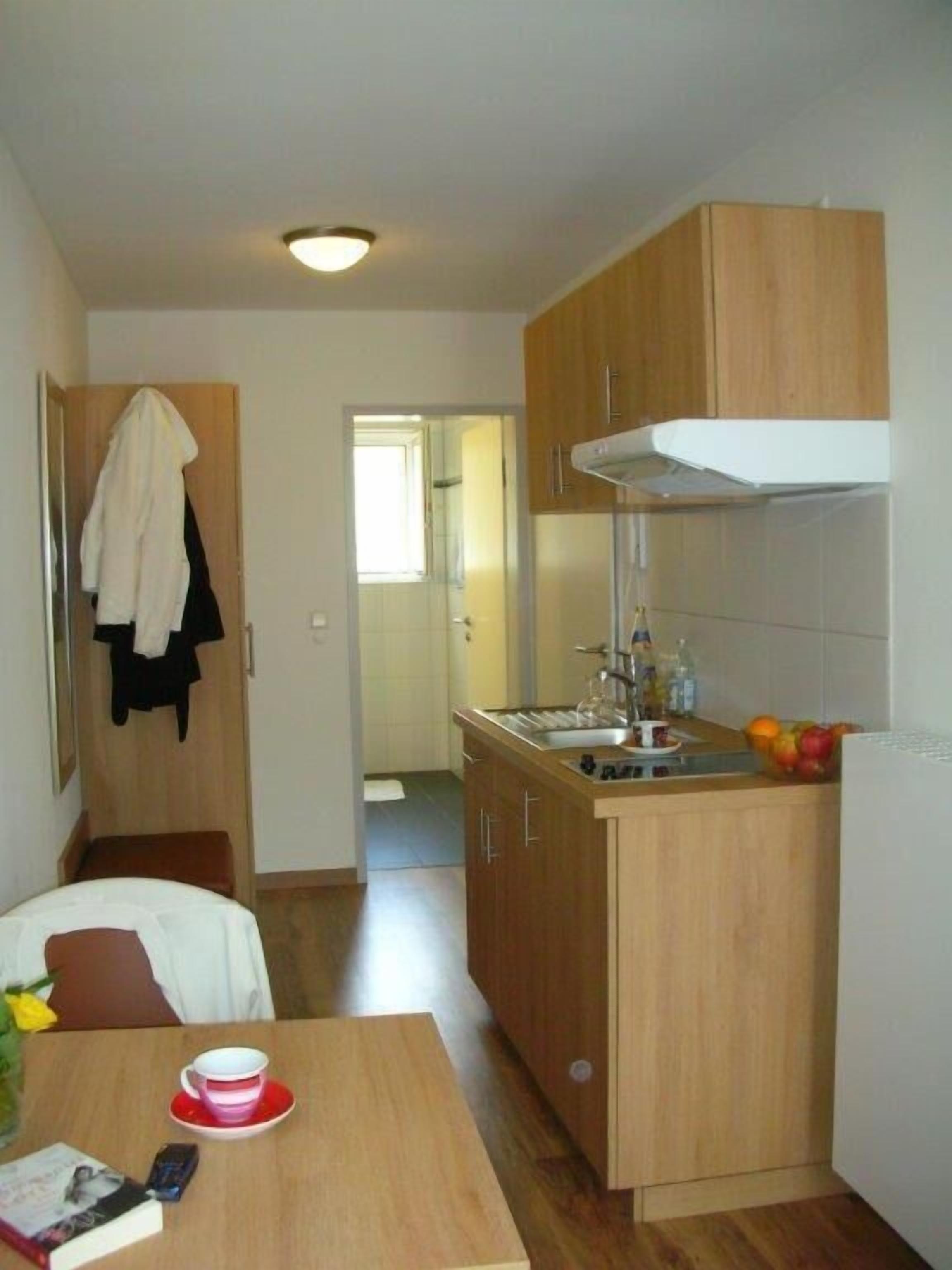 A compact kitchen with wooden cabinets, a sink, and a countertop. There is a dining table with a cup and a book.