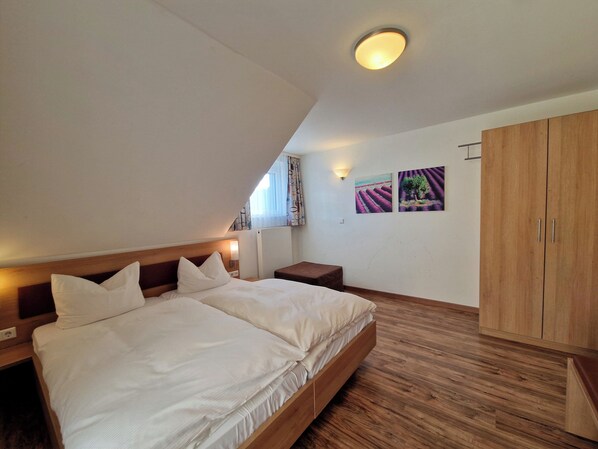 A bedroom with a large bed, wooden headboard, a nightstand, a wooden wardrobe, and a ceiling light. - Blume Hausach I Hotel & Restaurant (Hausach)