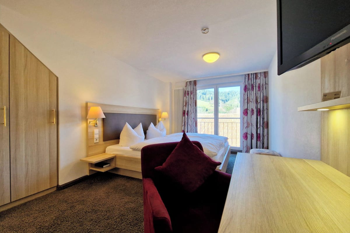 Une chambre d’hôtel équipée d’un lit, d’un bureau, d’une télévision et offrant une vue sur l’extérieur.