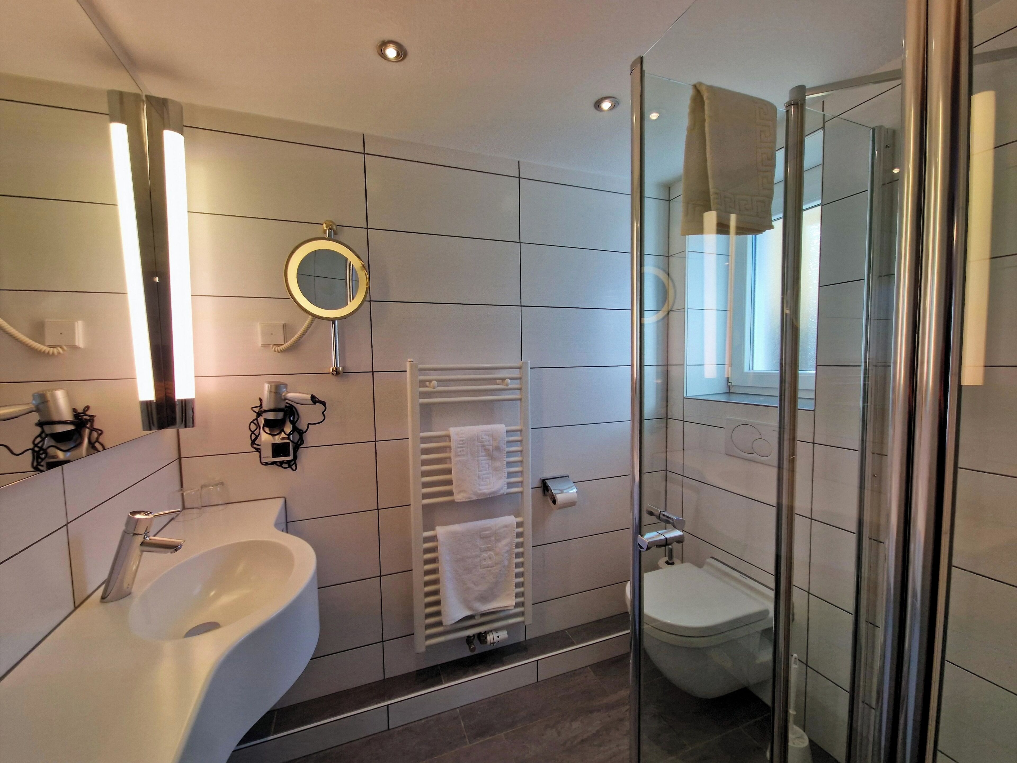A modern bathroom with a large sink, a mirror, a round mirror, a towel rack, and a glass shower enclosure.
