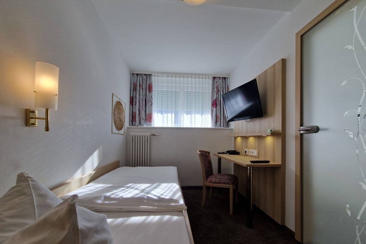 Une chambre d’hôtel avec un lit, un bureau, une chaise, une télévision et une fenêtre avec des rideaux.