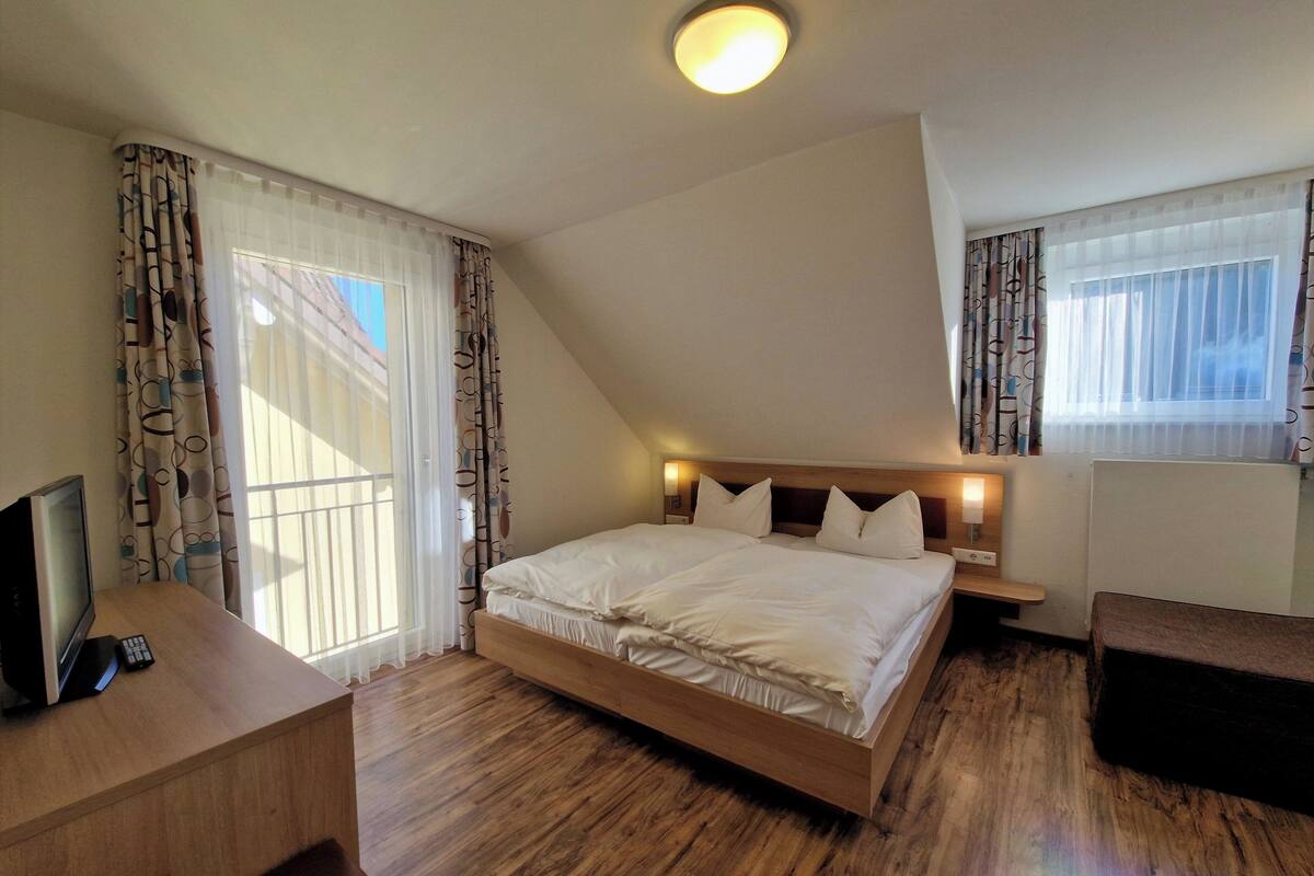 Une chambre avec un lit en bois, un bureau avec un ordinateur et une télévision.