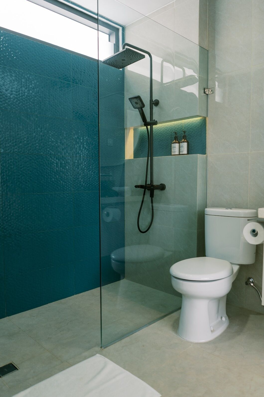 A modern bathroom with a glass shower enclosure, a toilet, and a shelf with toiletries.