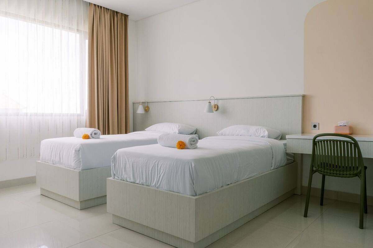 A hotel room with two beds, a desk, a chair, and a window with curtains.
