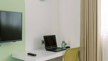 Una habitación moderna con un escritorio blanco, una computadora portátil, una silla, un televisor, un reloj y un aire acondicionado.