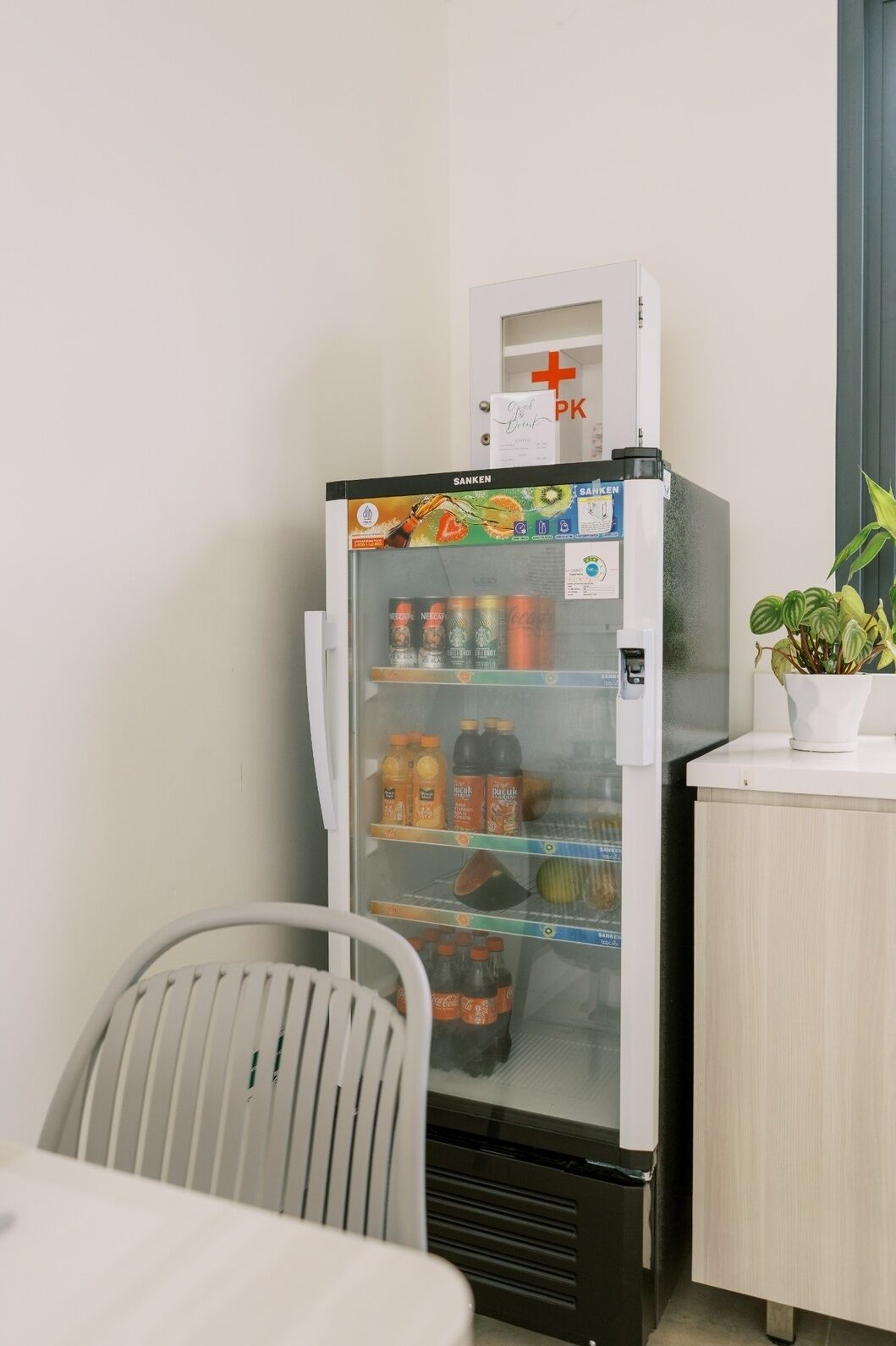 Un réfrigérateur rempli de boissons, une petite table avec une chaise et une plante en pot.