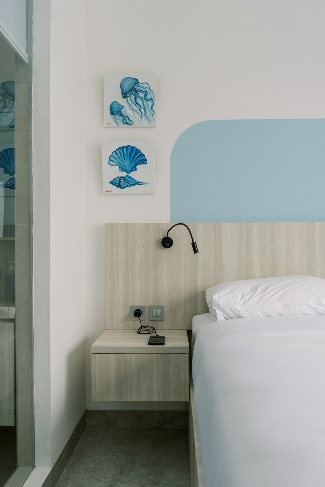 A hotel room with a bed, a nightstand with a lamp, and two wall art pieces.