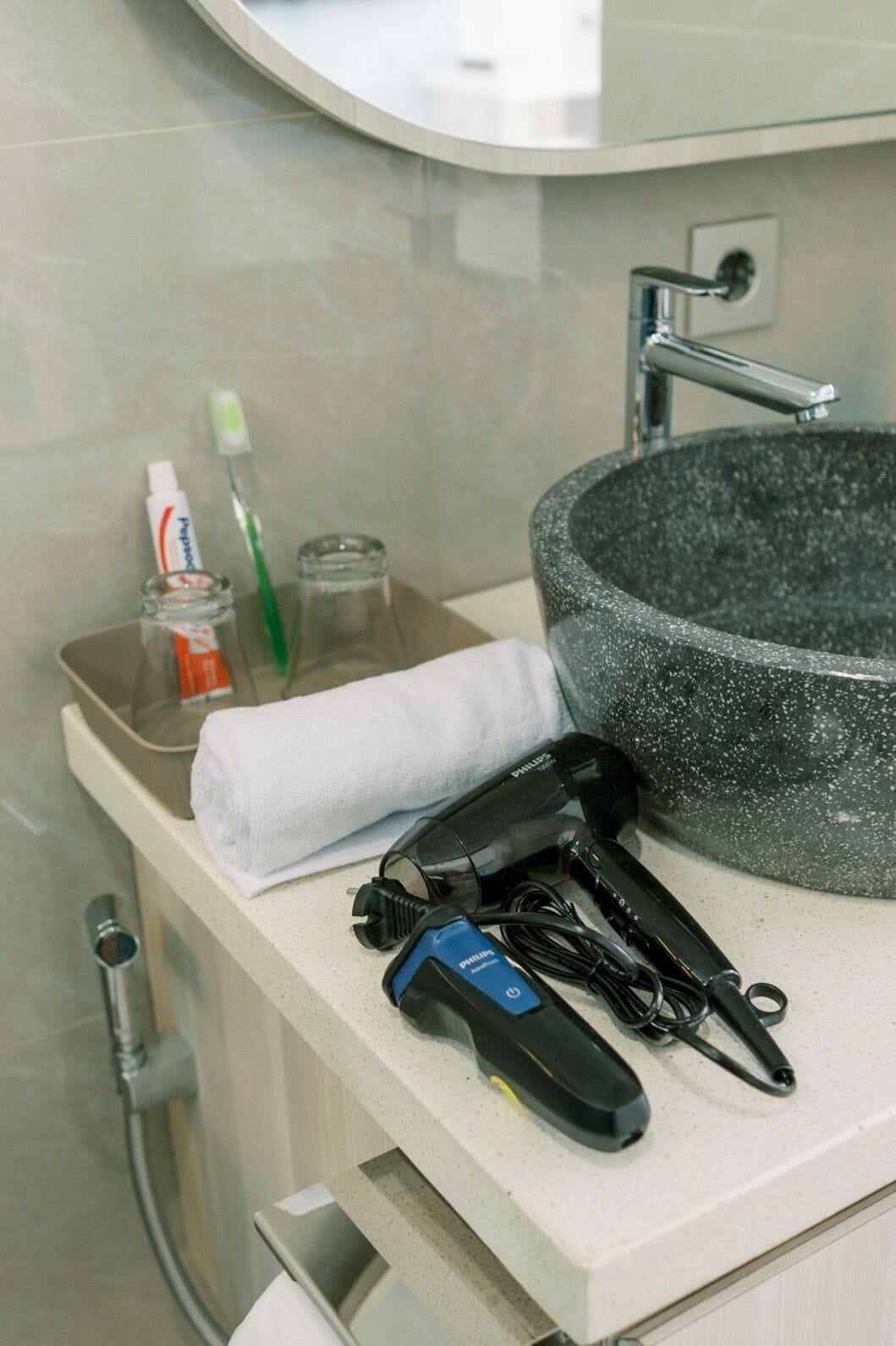 A bathroom with a round sink, a towel, a toothbrush, toothpaste, and a hairdryer.