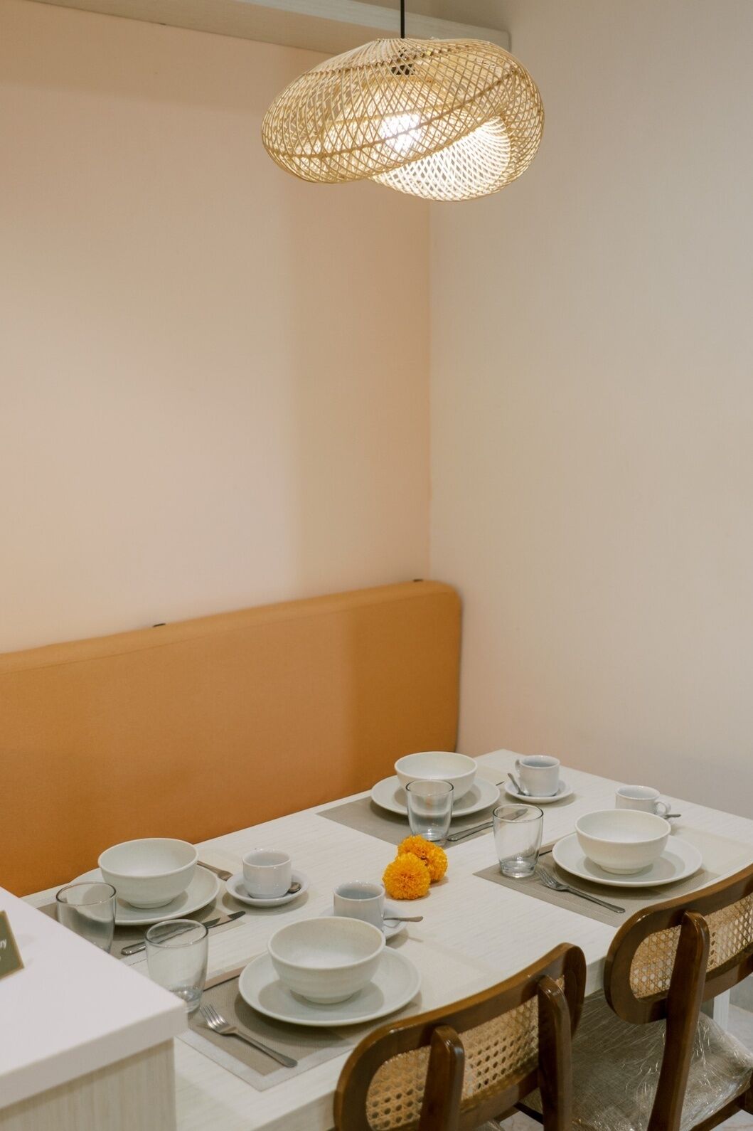 A dining area with a white table set for four, a woven pendant light, and a bench.