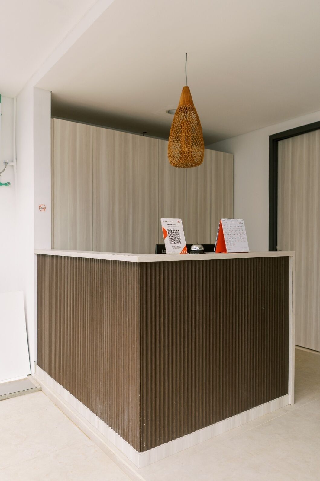 A reception desk with a woven pendant light, a notice board, and a door with a window.