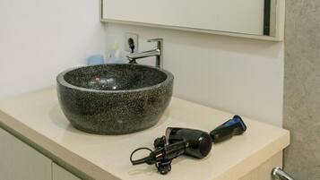 Un baño con lavamanos de piedra, espejo, secador de pelo y ducha.