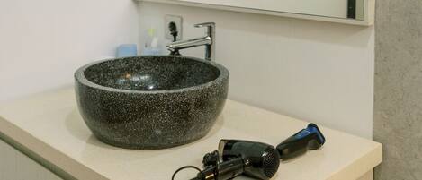 A bathroom with a stone sink, a mirror, a hairdryer, and a shower.