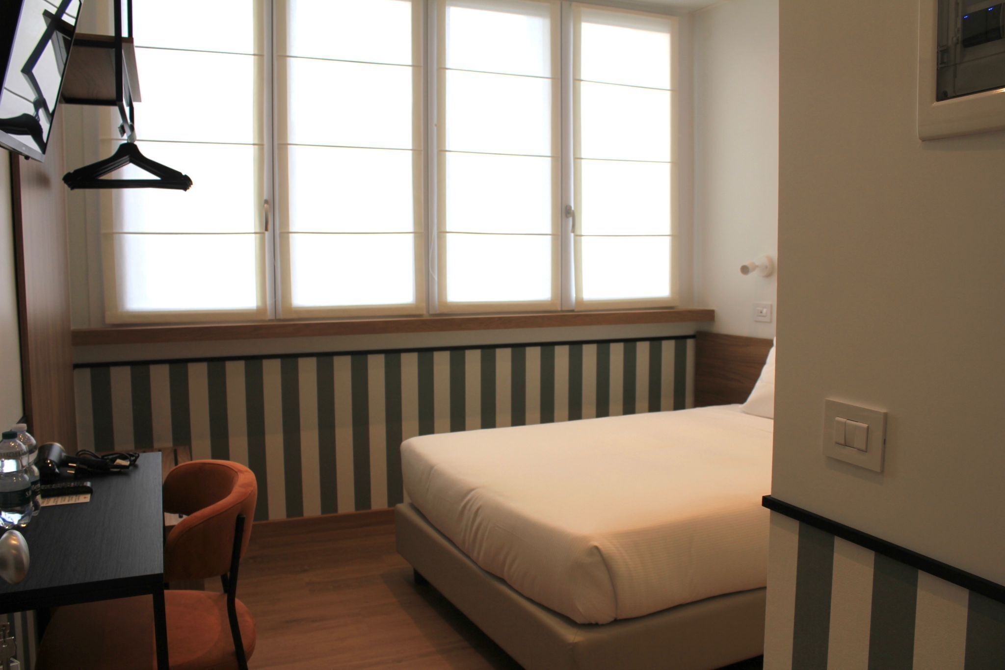 Un dormitorio con cama, escritorio y silla, ventana con persianas y radiador.