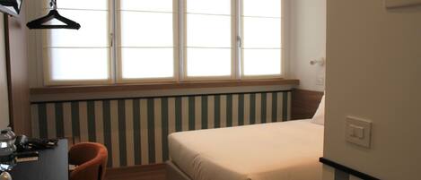 Un dormitorio con cama, escritorio y silla, ventana con persianas y radiador.