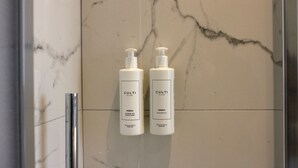 Dos botellas de gel de ducha y champú sobre una pared de mármol en un baño.