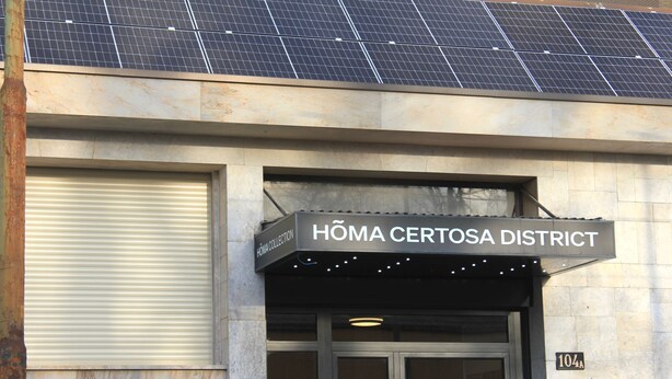 Un edificio con techo de paneles solares, un letrero que dice "HÖMA CERTOSA DISTRICT" y una puerta con persiana cerrada.