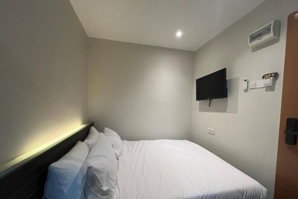 Une chambre d’hôtel équipée d’un lit, d’un téléviseur à écran plat fixé au mur, d’un thermostat et d’une porte avec une poignée.