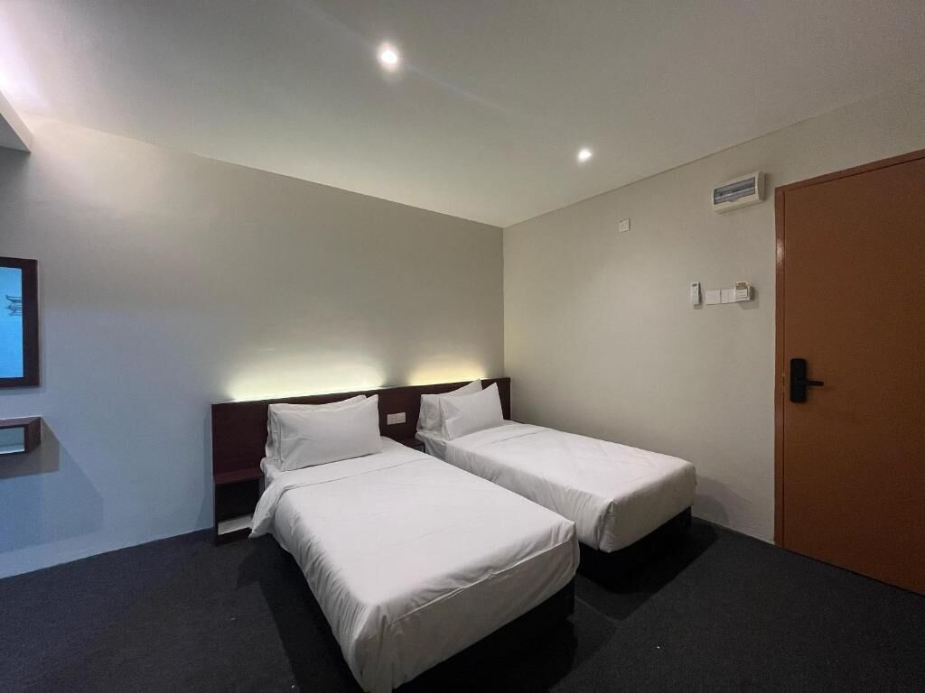 A hotel room with two single beds, a wooden headboard, a small bedside table, a wall-mounted TV, and a door with a handle.