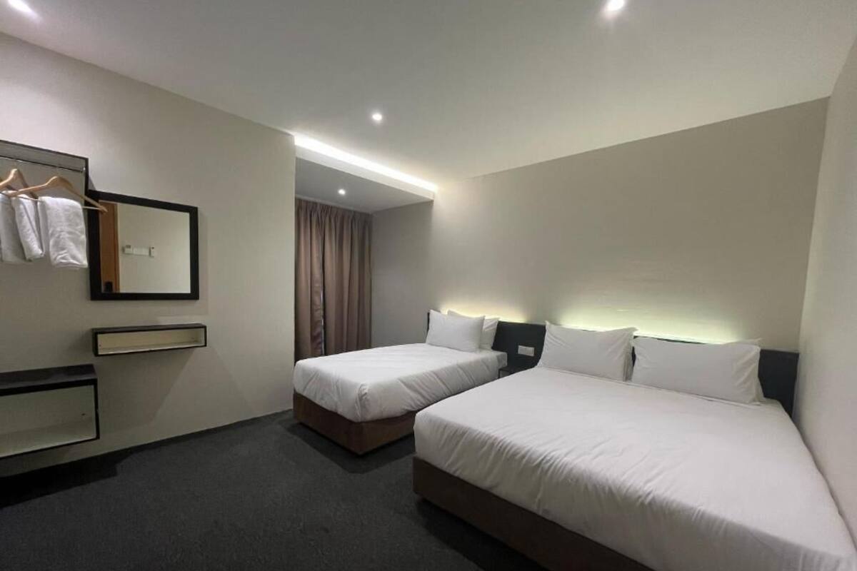 Une chambre d’hôtel avec deux lits, un miroir, une armoire et une salle de bain visible par une porte.