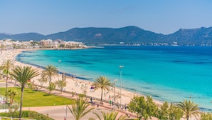 Eine Küstenlandschaft mit klarem türkisblauem Wasser, Palmen und einer Stadtansicht im Hintergrund.