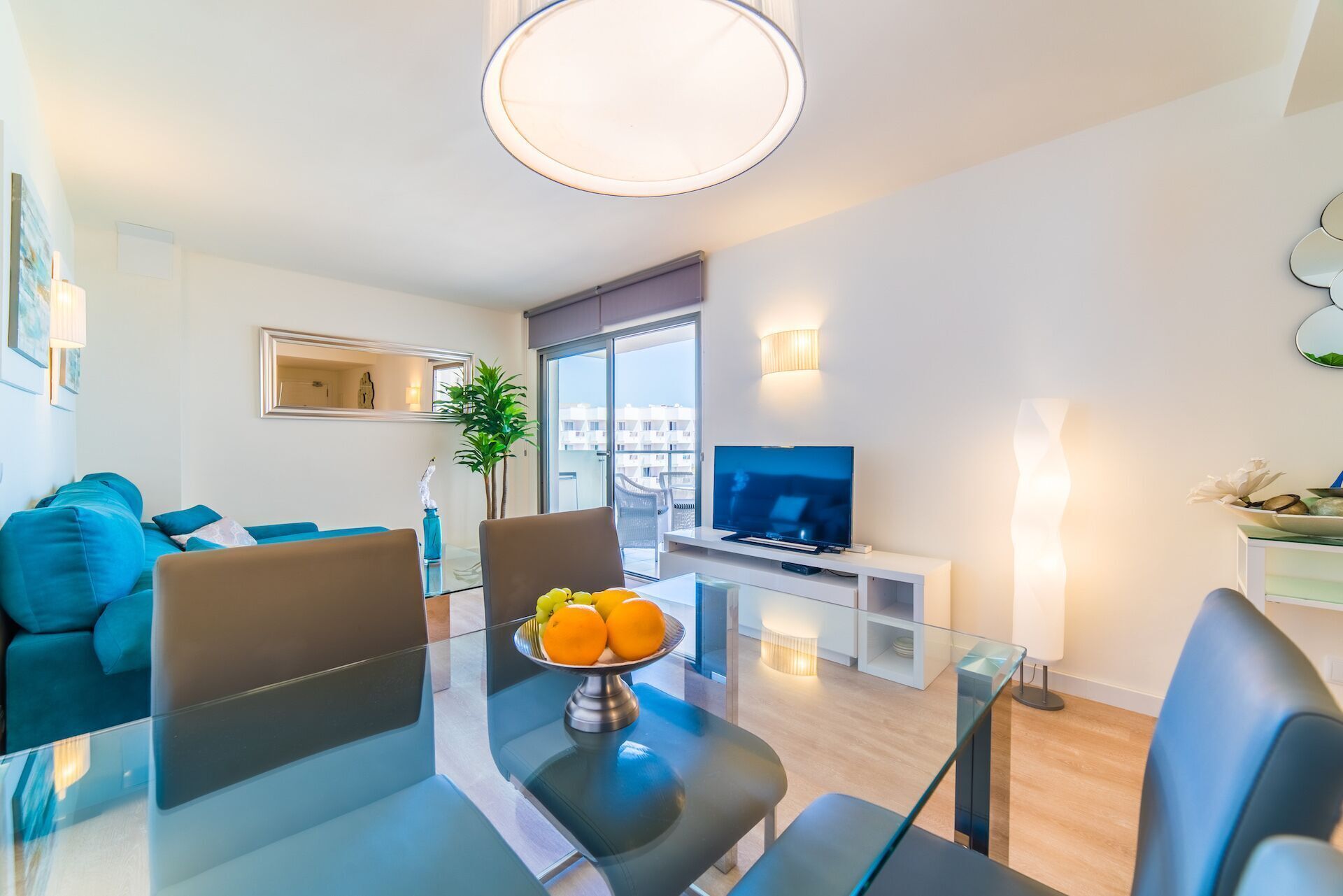 En moderne stue med et glasbord, et fladskærms-tv og en balkon med udsigt til bygninger.