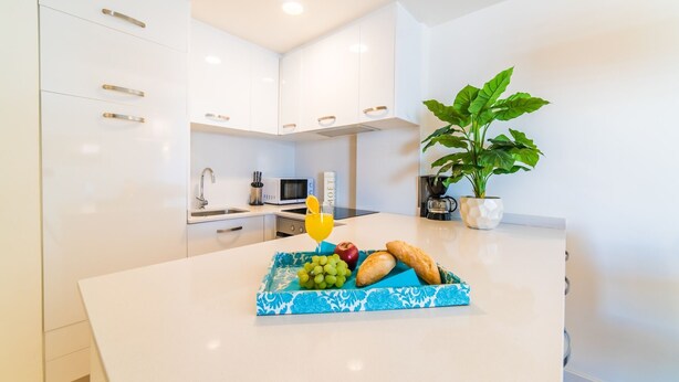 A modern kitchen with white cabinets, a microwave, and a sink. There is a tray with fruits and bread on the counter. - Cala Millor, beautiful apartment, 6 floor, 2 bedrooms, sea view, directly at the beach WIFI (Sant Llorenç des Cardassar)