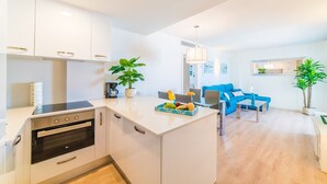 Eine moderne Küche mit weißen Schränken, einem eingebauten Backofen und einem Essbereich mit einem blauen Sofa sowie einem Tisch, der mit Früchten und einer Kaffeemaschine gedeckt ist.
