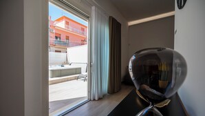 A modern hotel room with a sliding glass door leading to a balcony, a small seating area, and a decorative mirror. - Mediterranea Suite (Avola)