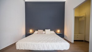 A bedroom with a large bed, two bedside tables with lamps, and a walk-in closet. - Mediterranea Suite (Avola)