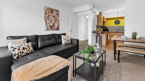 A modern living room with a black leather sofa, a glass coffee table, and a large painting of a lion. - Modern 2-Bed Flat with Flexible Beds (Warrington)