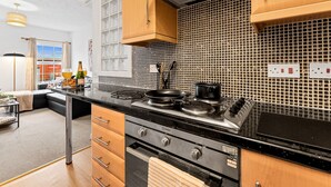 A modern kitchen with a black countertop, stainless steel appliances, and wooden cabinets. - Modern 2-Bed Flat with Flexible Beds (Warrington)