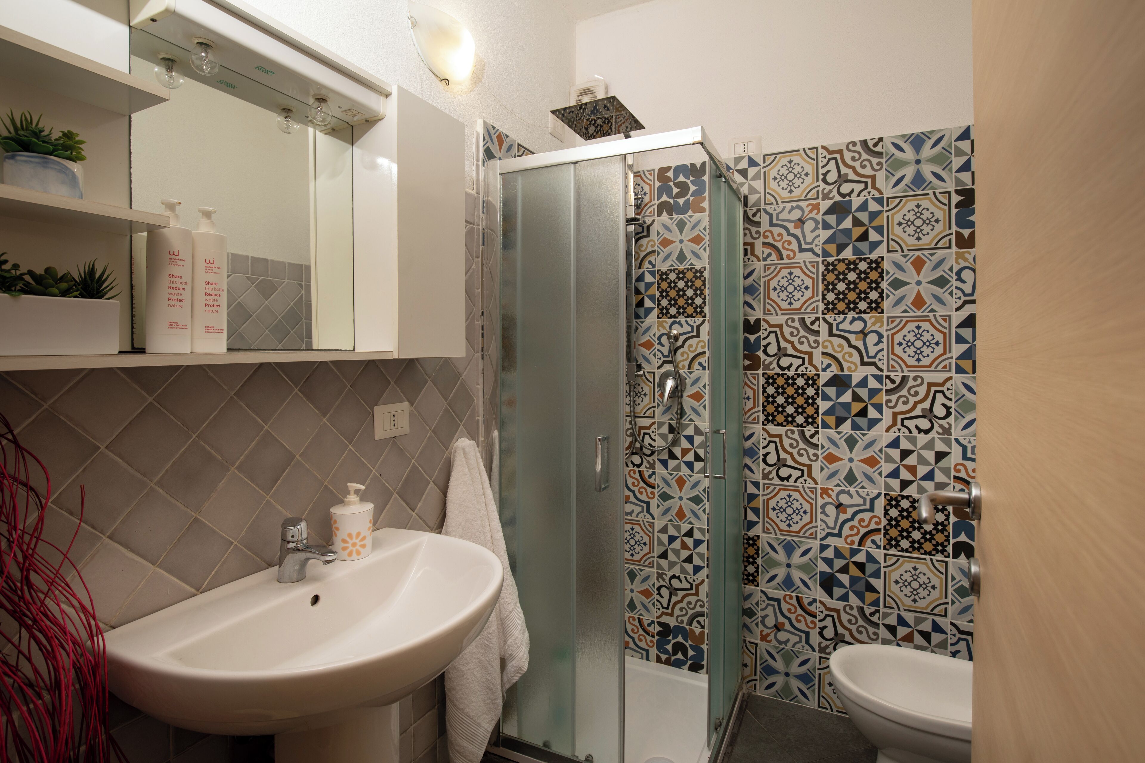 A bathroom with a glass-enclosed shower, a white sink, and a tiled shower wall.