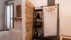 Een kleine kamer met een bed, een houten wand, een zwart metalen plank met een waterkoker, een magnetron en een witte koelkast.