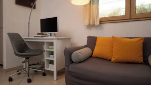 Een kamer met een bureau, computer, kantoorstoel en een bank met kussens.